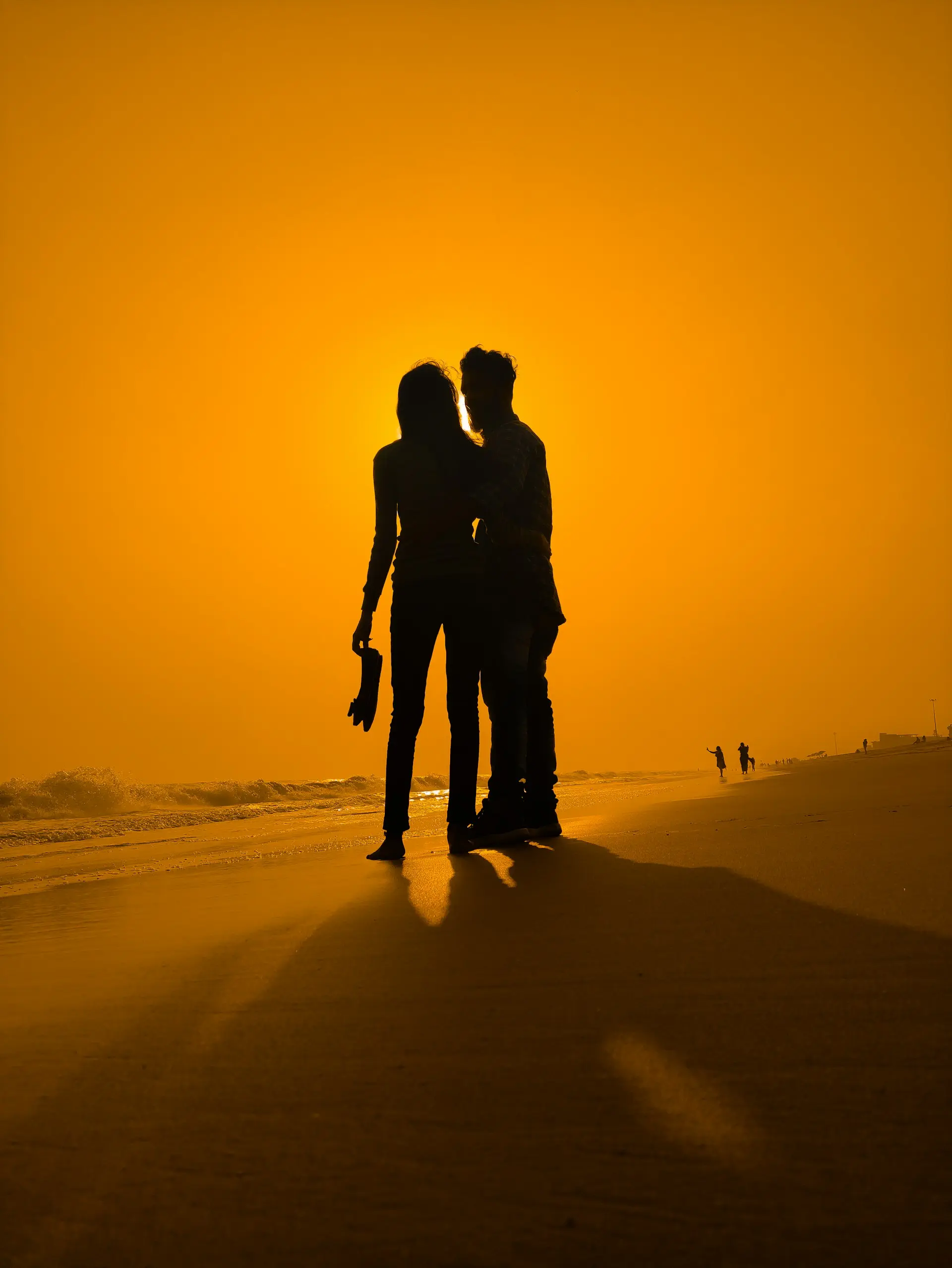 Couple silhouette walking along a beach at amber sunset